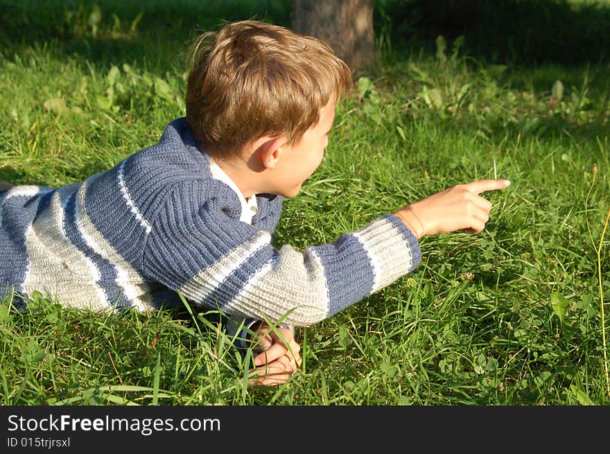 The boy lies on a grass and points a finger