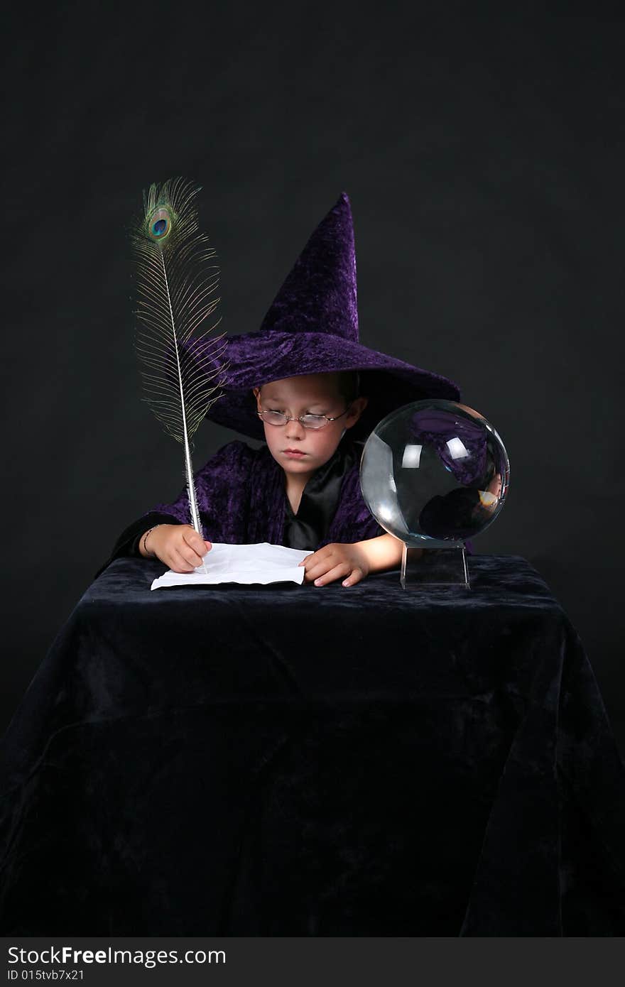 Wizard child next to crystal ball writing a spell with a peacock feather pen. Wizard child next to crystal ball writing a spell with a peacock feather pen