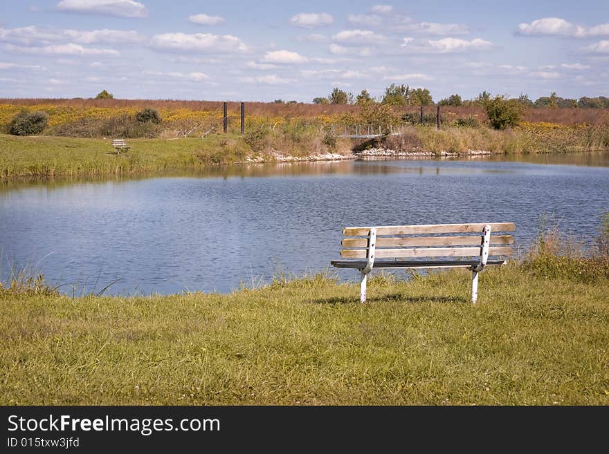 Wooden bench overlooking blue lake in early autumn day. Wooden bench overlooking blue lake in early autumn day