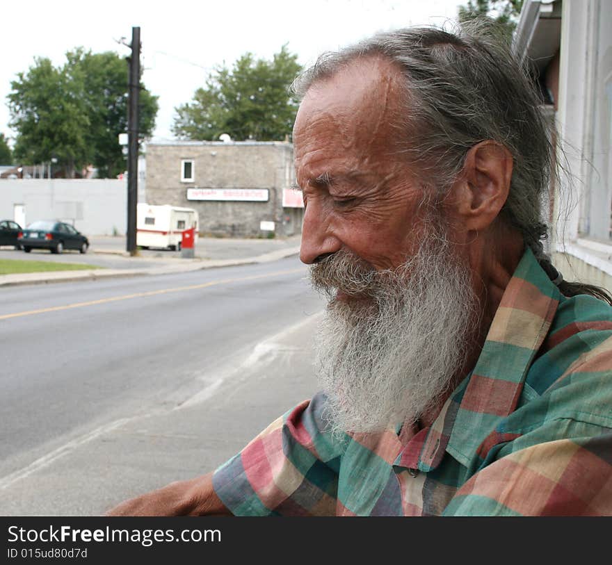 A senior male is sitting down outdoors being very pensive. A senior male is sitting down outdoors being very pensive