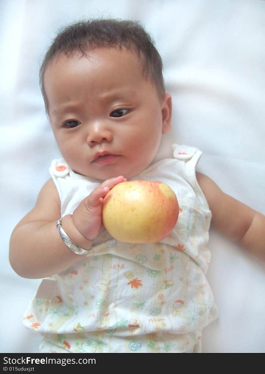 Pretty baby and red apple on a bed