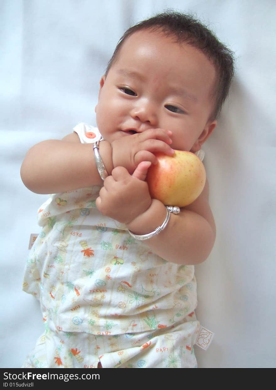 Pretty baby and red apple on a bed