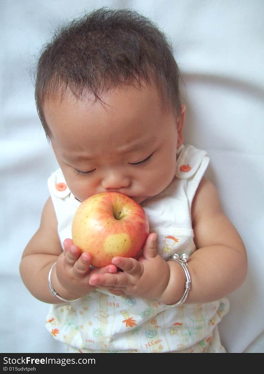 Pretty baby and red apple on a bed