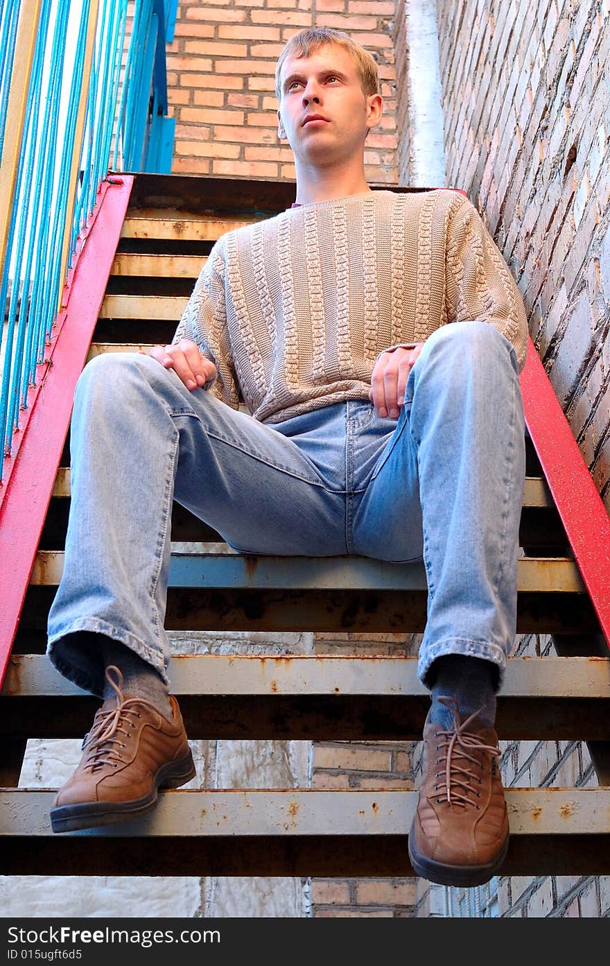 Young stylish man with blonde hair sit on stairs near brick wall. Young stylish man with blonde hair sit on stairs near brick wall.