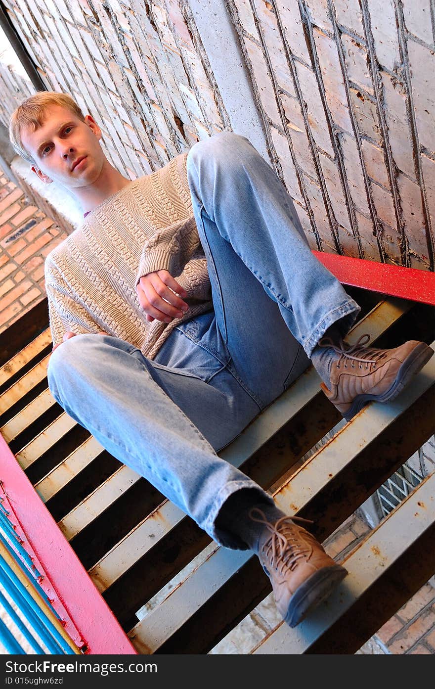 Young stylish man with blonde hair sit on stairs near brick wall. Young stylish man with blonde hair sit on stairs near brick wall.