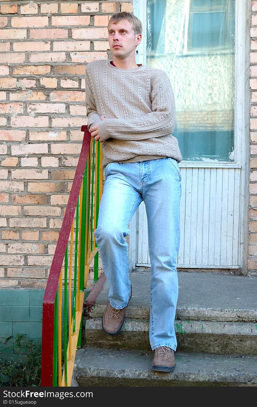 Young stylish man with blonde hair stay on stairs near brick wall. Young stylish man with blonde hair stay on stairs near brick wall.