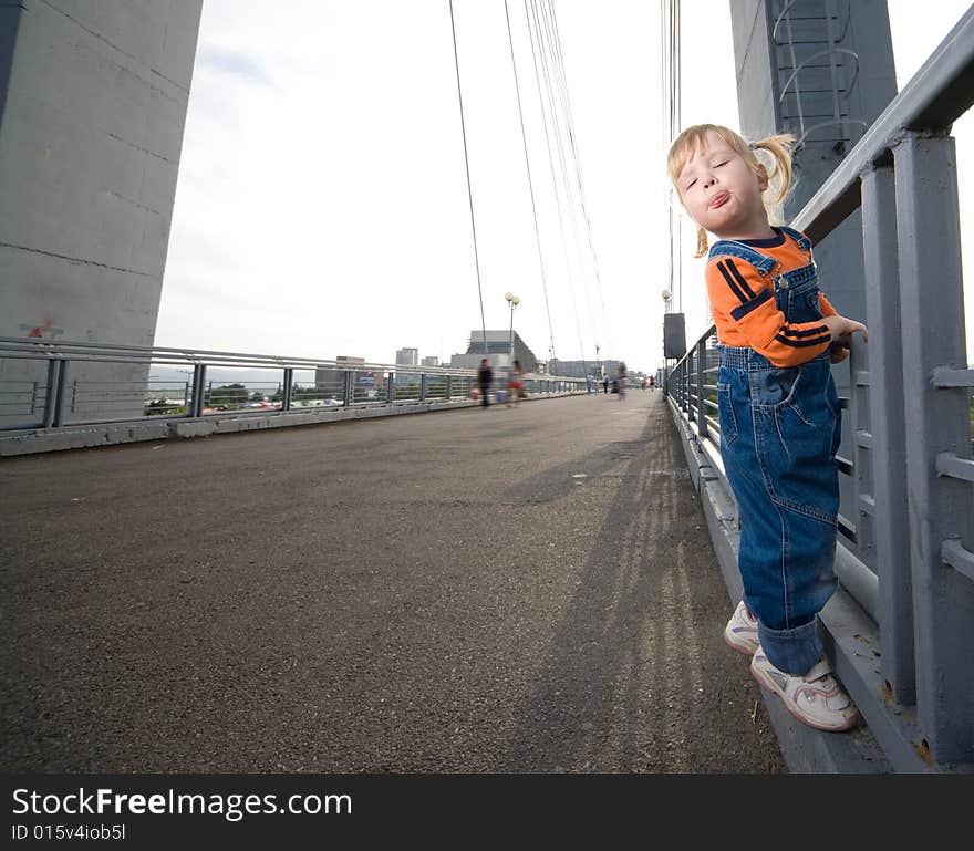 Little girl show tongue hold to fence on bridge