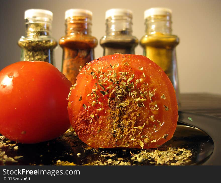 Ripe tomato cut on half with pepper, oregano, curry and red paprika on it and standing behind. Ripe tomato cut on half with pepper, oregano, curry and red paprika on it and standing behind.