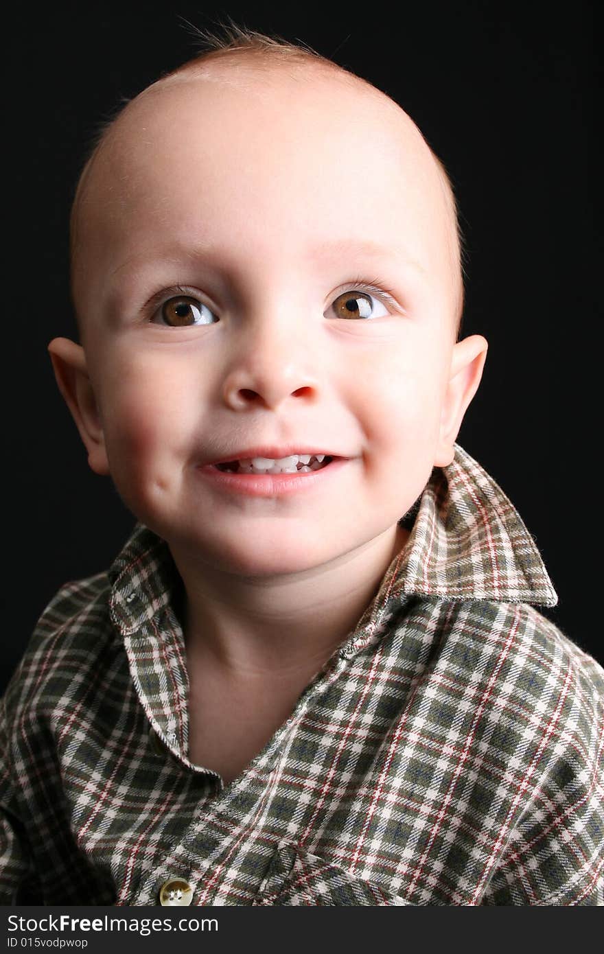 Blonde toddler against a black background with a big smile