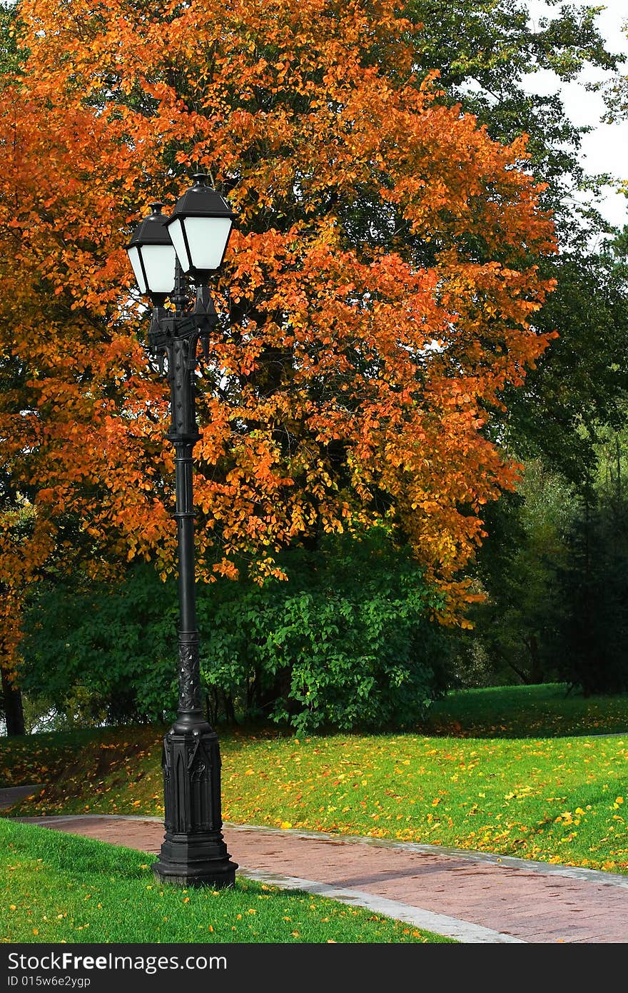 An autumn time, trees in yellow leaves, below a green grass, in the foreground a lantern. An autumn time, trees in yellow leaves, below a green grass, in the foreground a lantern