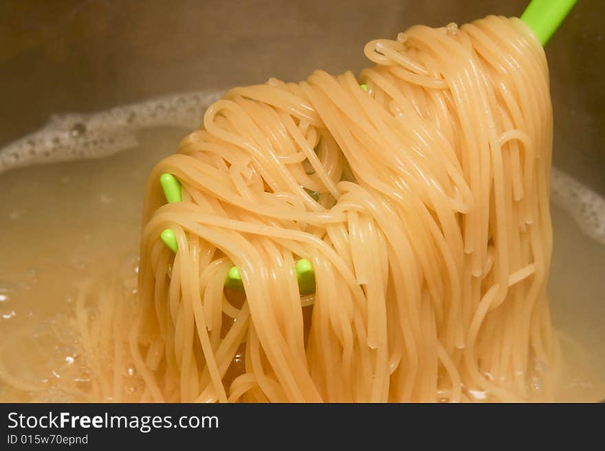 Spaghetti on a green spoon are pulled out of boiling water. Spaghetti on a green spoon are pulled out of boiling water