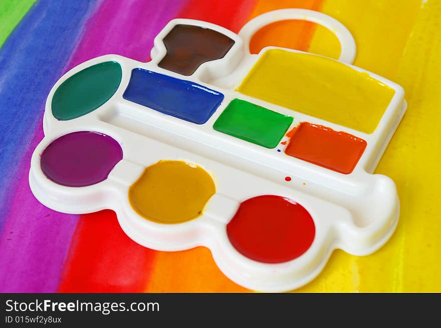 Box of watercolors and a brush on a colorful  background.