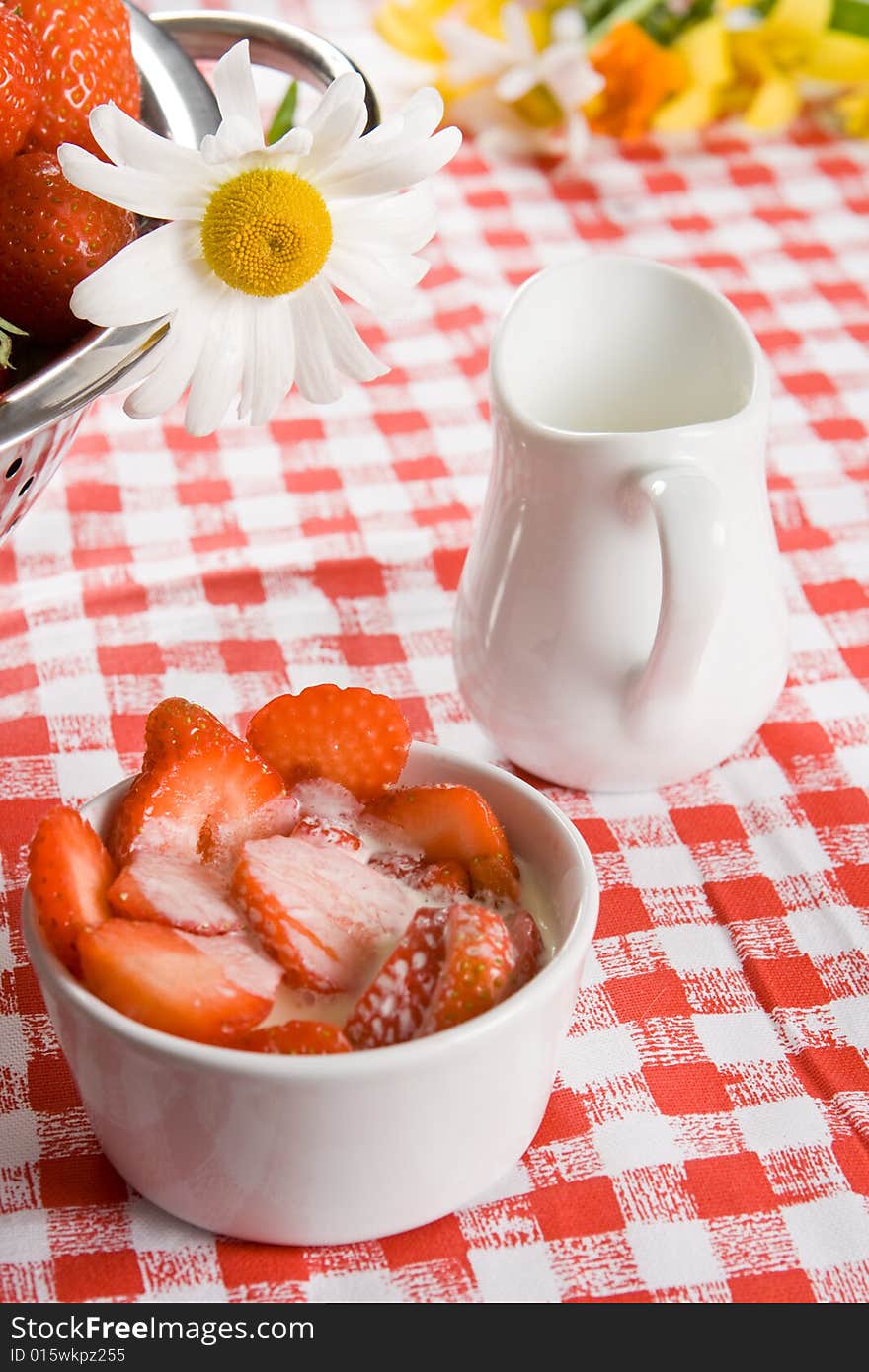 Sliced strawberries and cream in a white pot with a daisy on a red and white cloth