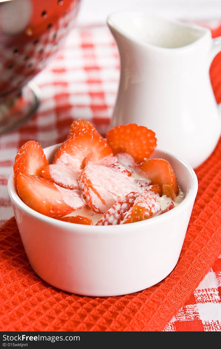 Fresh sliced strawberries with cream in a white pot on a red cloth