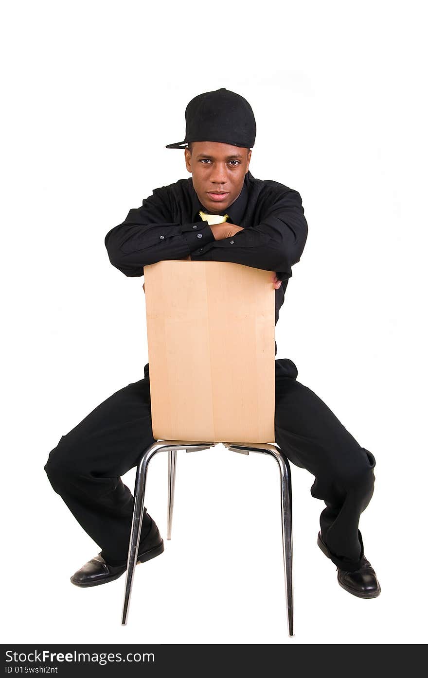 Young man straddles chair in dress clothes and baseball cap. Young man straddles chair in dress clothes and baseball cap