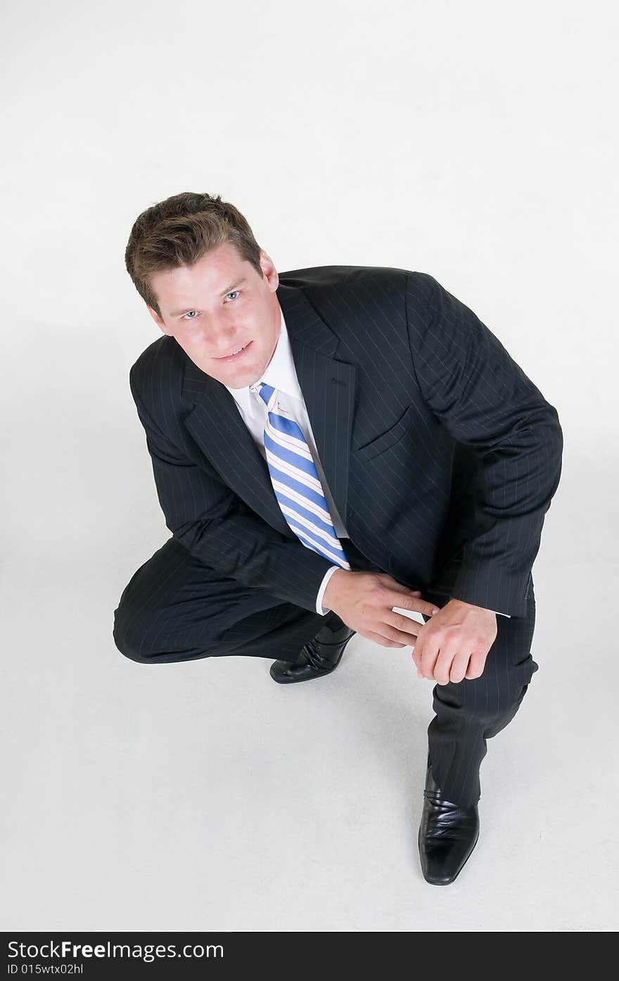 Young businessman squats down on grey background. Young businessman squats down on grey background