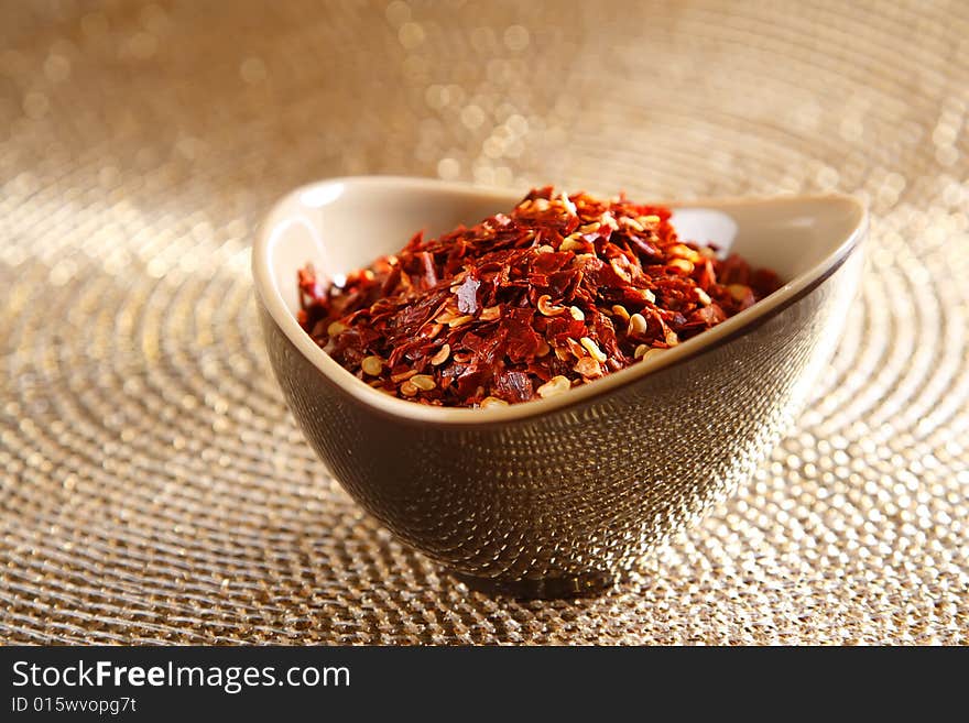 Crushed red hot chilli pepper in bowl on golden glitter background, shallow DOF