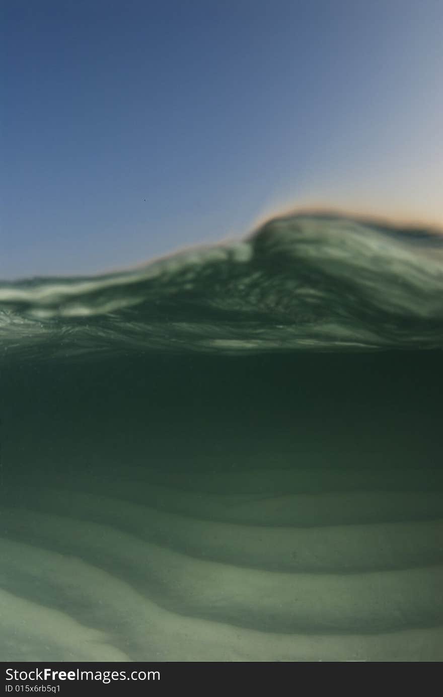 Curl of a passing wave on an underwater/overwater shot image with the blue sky and color from the setting sun rim lighting the wave. Curl of a passing wave on an underwater/overwater shot image with the blue sky and color from the setting sun rim lighting the wave.