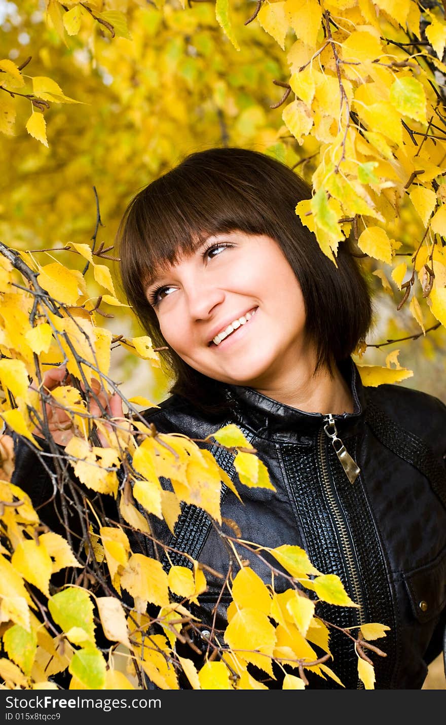 Cheerful cute girl in the park looking at yellow leaves