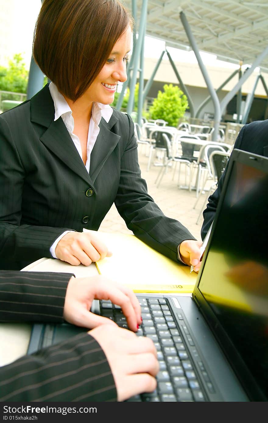 Show of smiling business woman writing with hand of other woman typing on laptop on foreground. Show of smiling business woman writing with hand of other woman typing on laptop on foreground