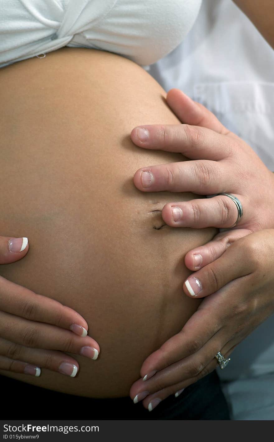 Young expectant parents sitting, looking at her abdomen. Young expectant parents sitting, looking at her abdomen