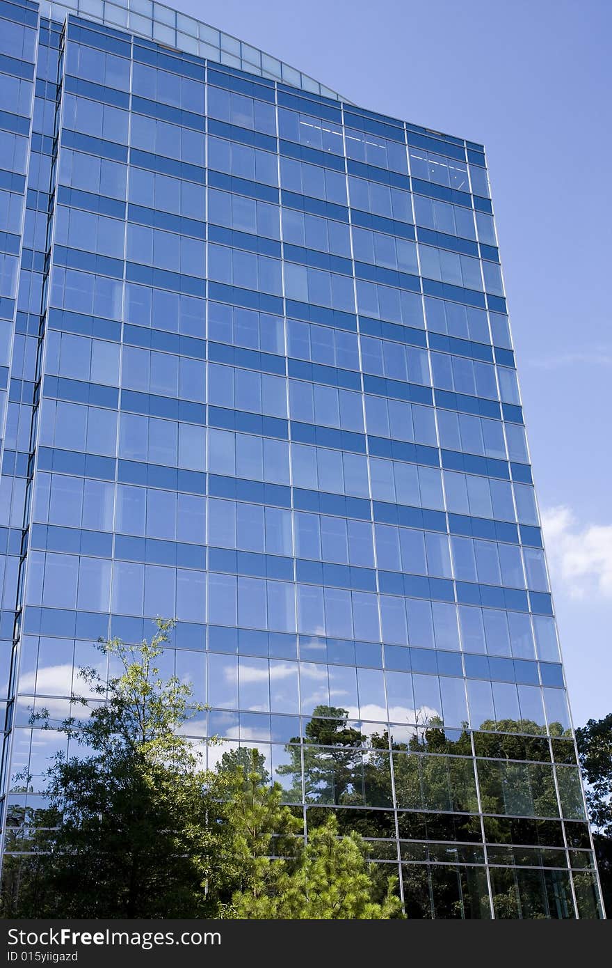 A blue glass office tower with clouds and trees reflected