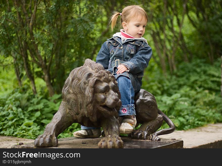 Small funny girl sitting on lion sculpture at the park. Small funny girl sitting on lion sculpture at the park