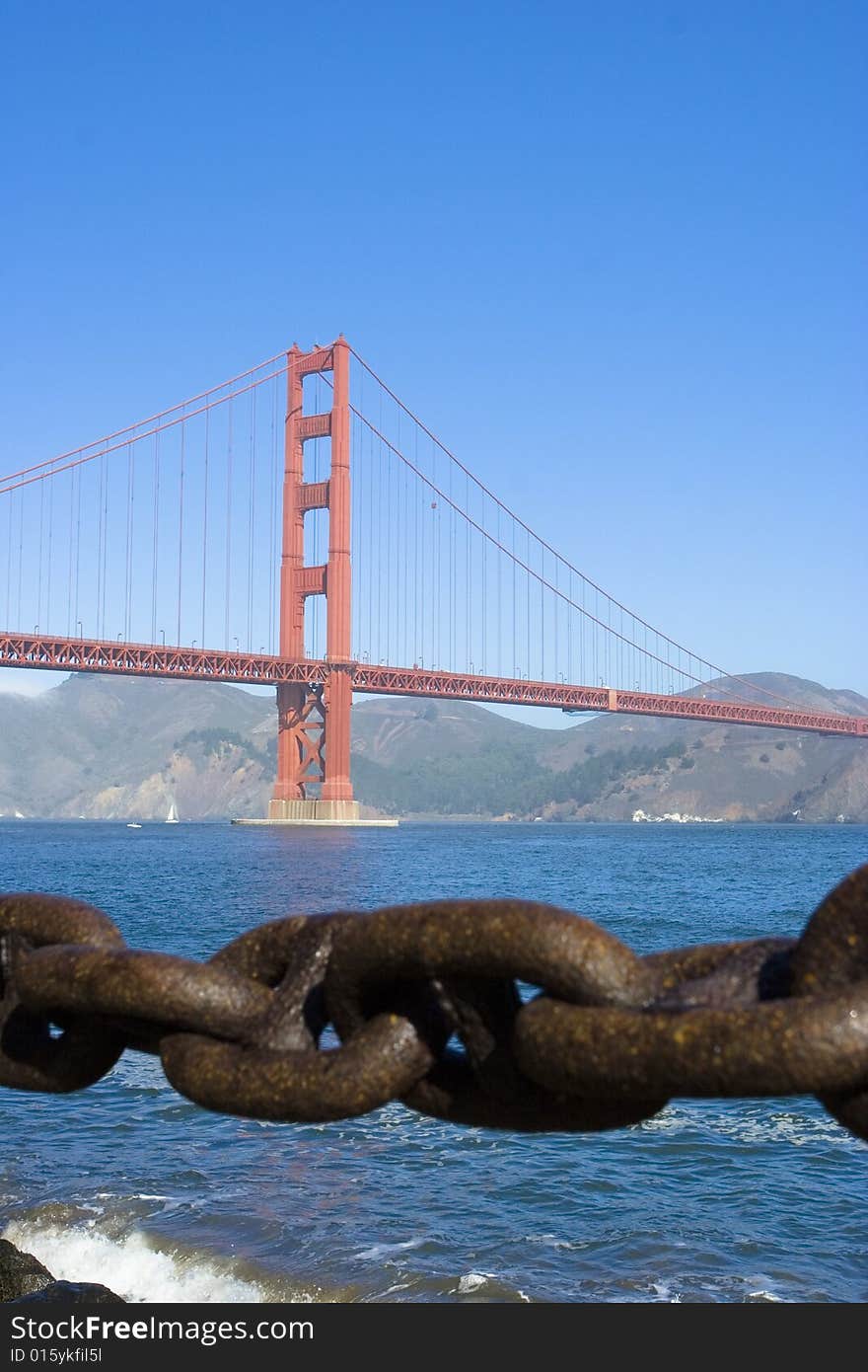 A photo with the focus on a chain with a bridge in the rear