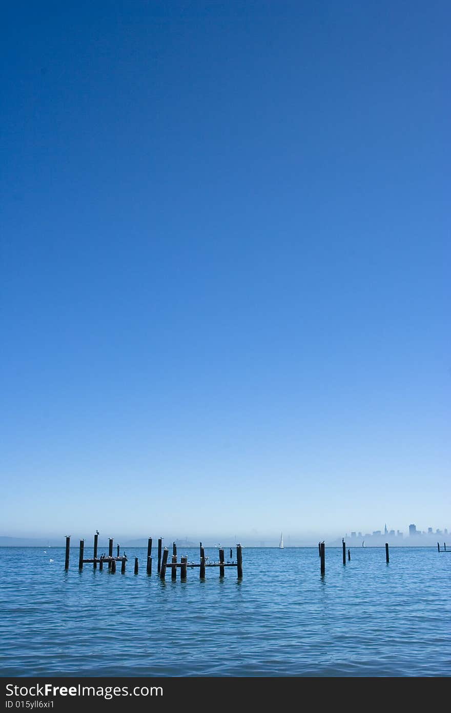 Poles in the water with the city on the background that is surrounded by fog