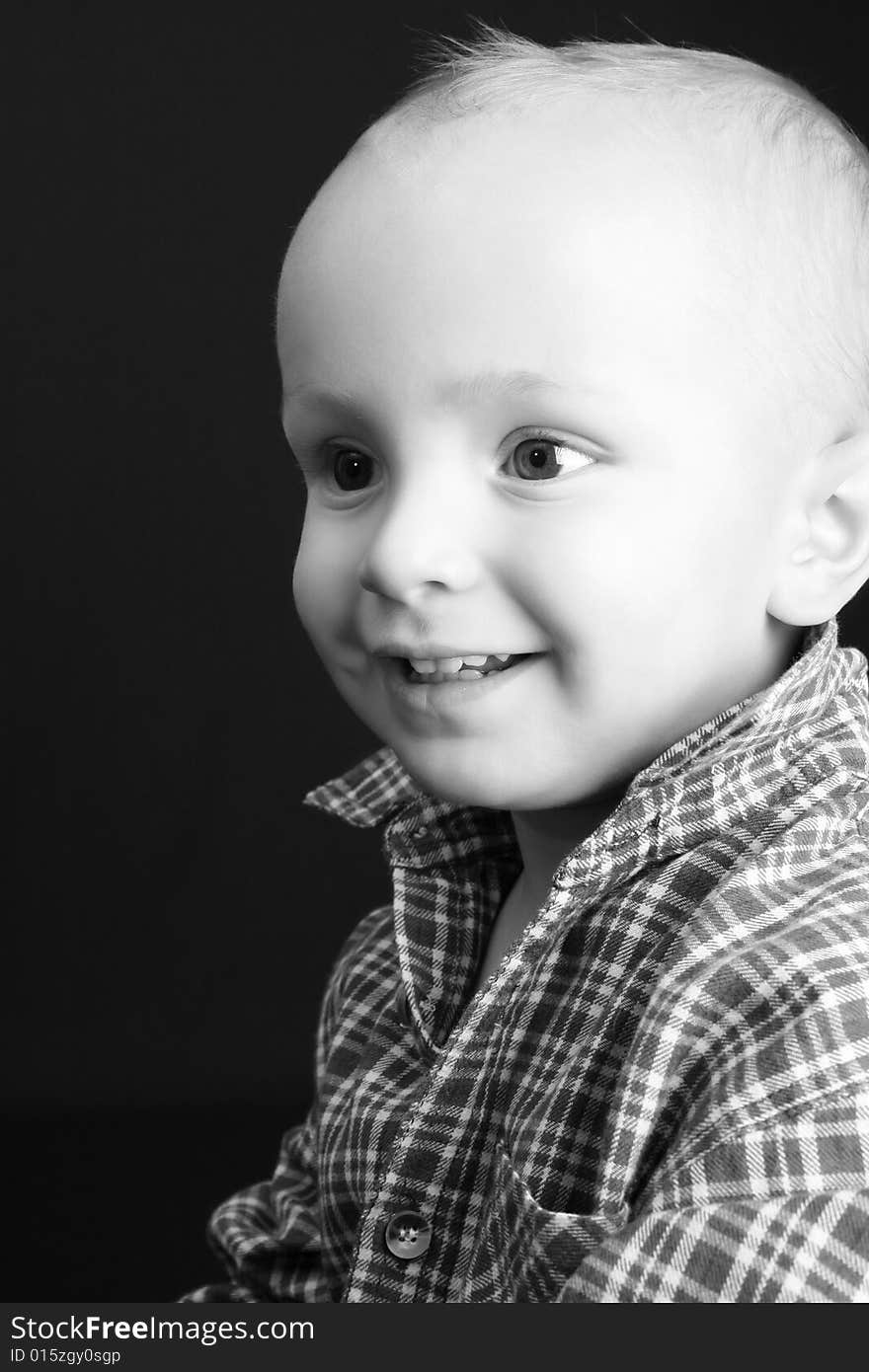 Blonde toddler against a black background with a big smile