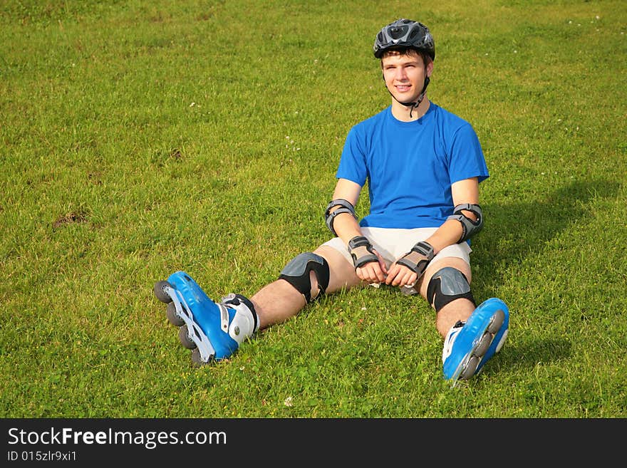 Guy in rollerblades sits on green grass. Guy in rollerblades sits on green grass