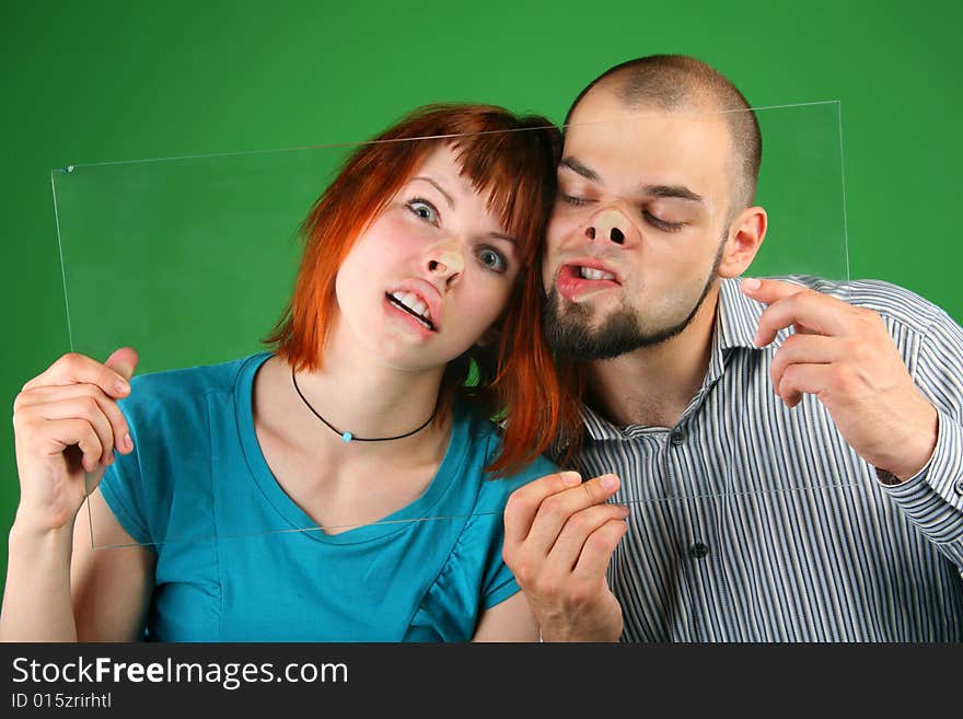 Close up girl with red hair and guy grimace behind glass on green