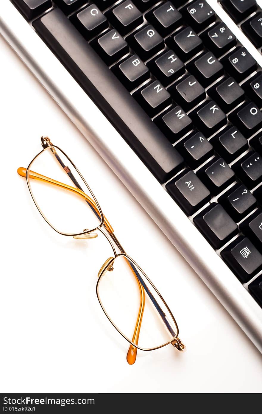 Fragment of keyboard with glasses, white background