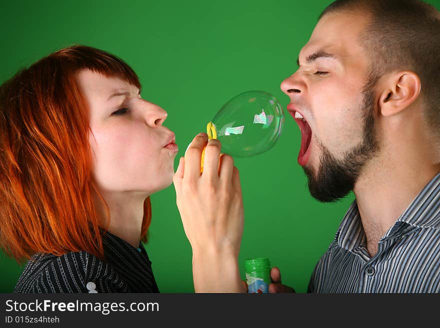 Girl with red hair blows soap bubble in mouth to guy on green. Girl with red hair blows soap bubble in mouth to guy on green