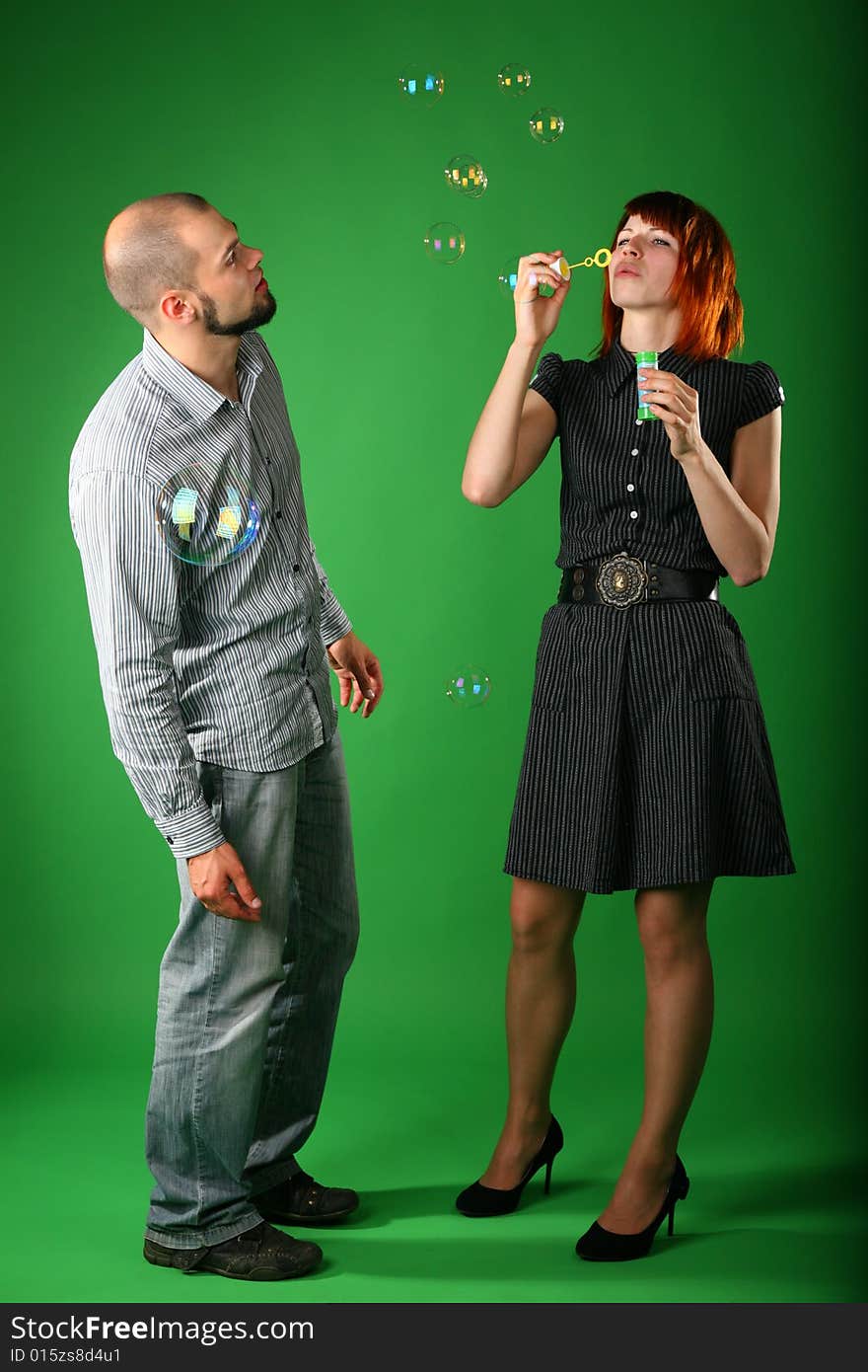 Girl with red hair blows soap bubbles, and guy looks at it on green. Girl with red hair blows soap bubbles, and guy looks at it on green