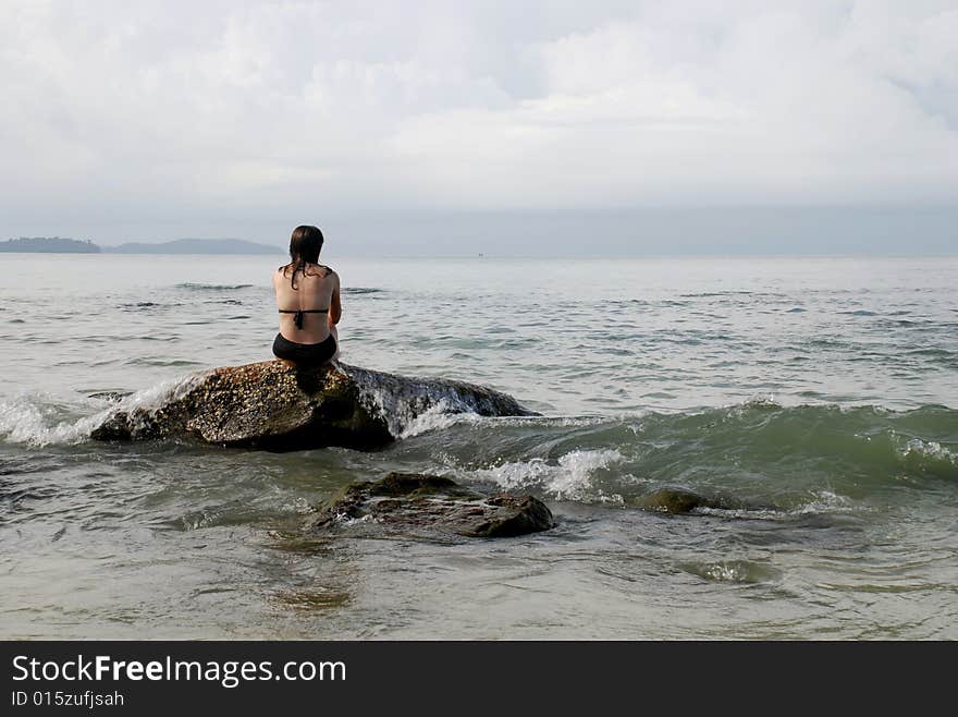 A woman sitting on a rock near the beach resort of Sihanoukville, Cambodia as waves from the South China Sea wash over her. A woman sitting on a rock near the beach resort of Sihanoukville, Cambodia as waves from the South China Sea wash over her.