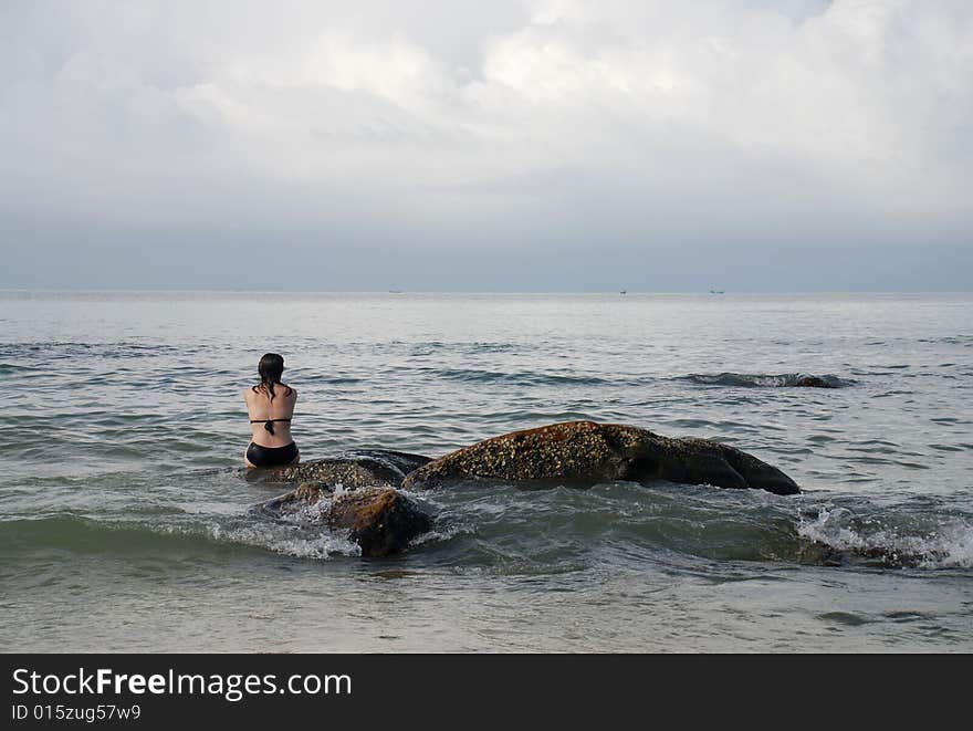 A woman sitting on a rock near the beach resort of Sihanoukville, Cambodia, watching the waves come in from the South China Sea.