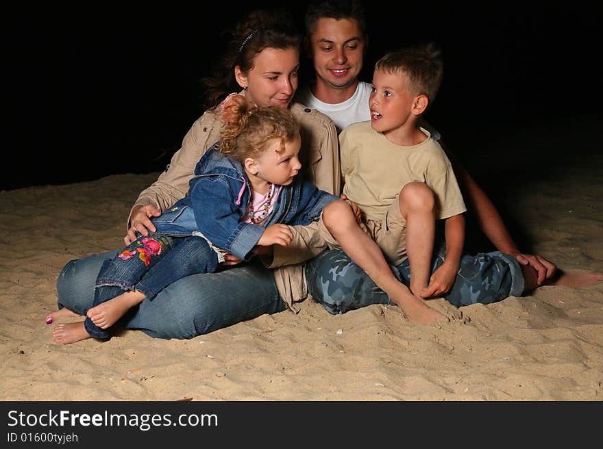 Parents With Children Sit On Sand At Night