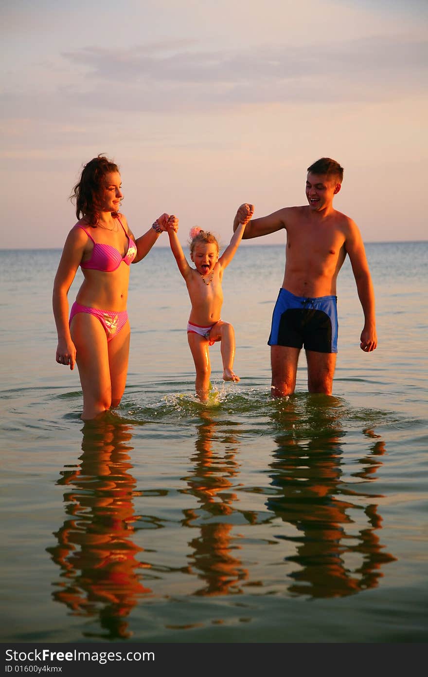 Parents hold daughter for hands in sea, summer