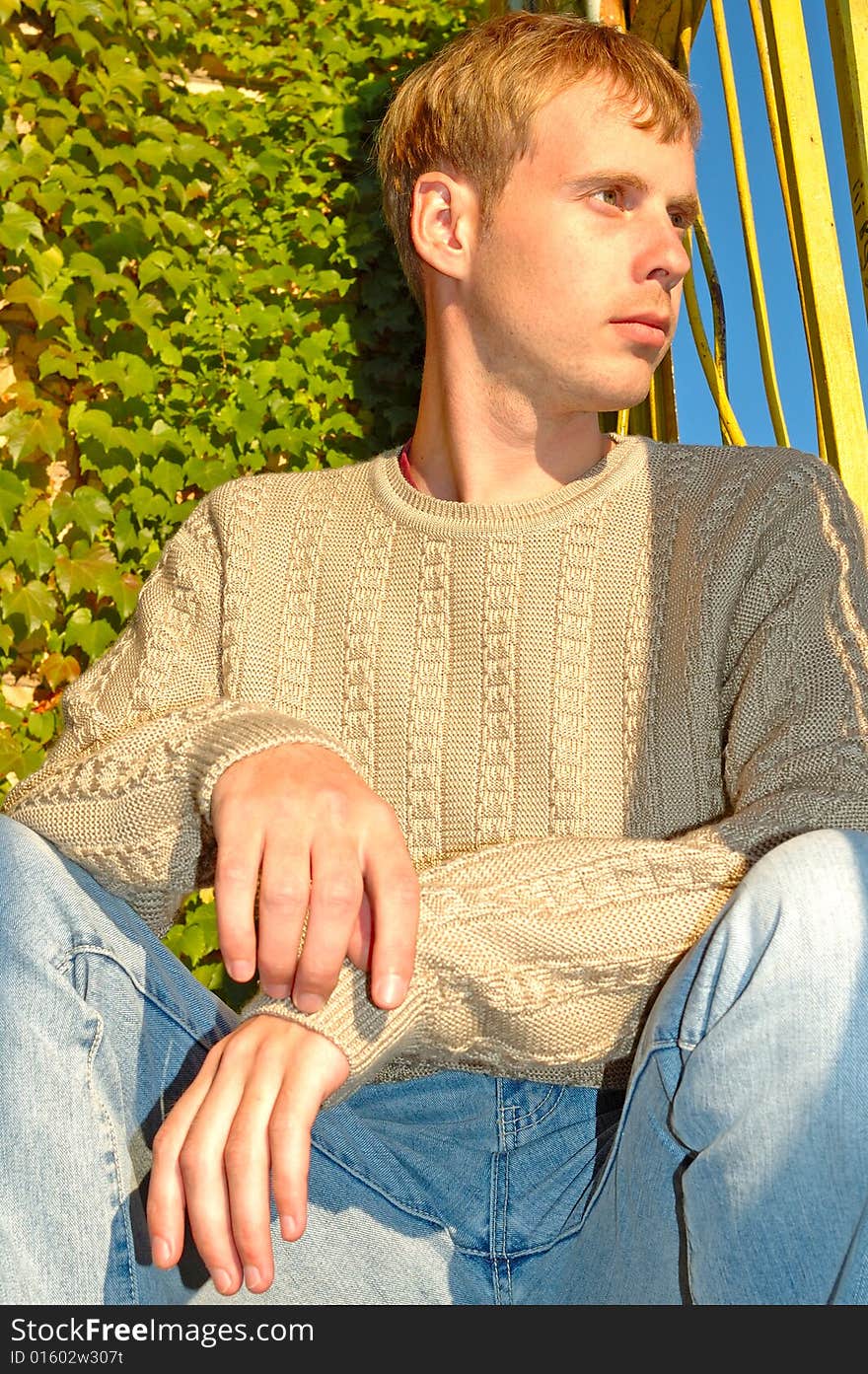 Young stylish man sit near overgrown wall.