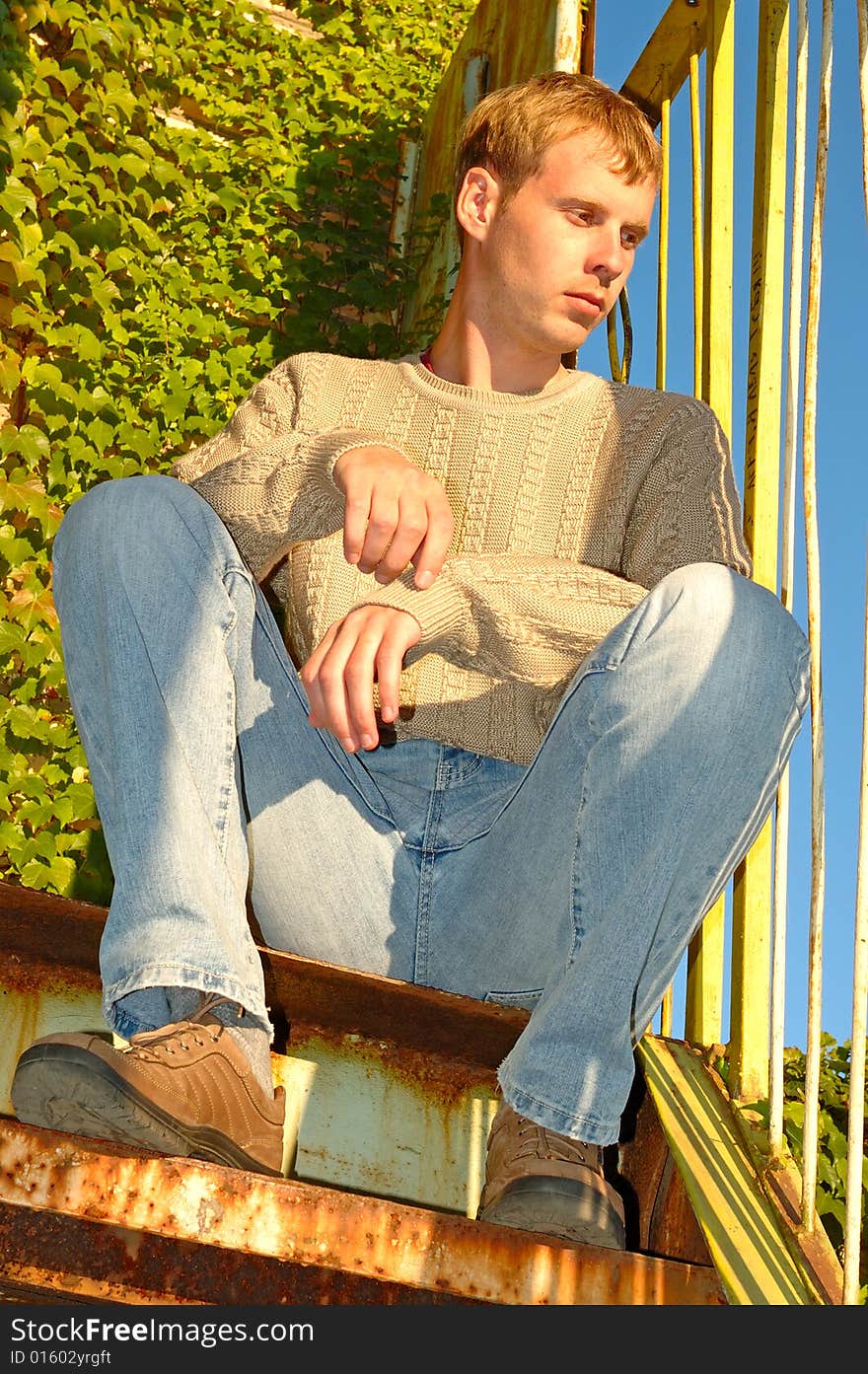 Young stylish blonde man sit on stairs near overgrown with vine wall. Young stylish blonde man sit on stairs near overgrown with vine wall.