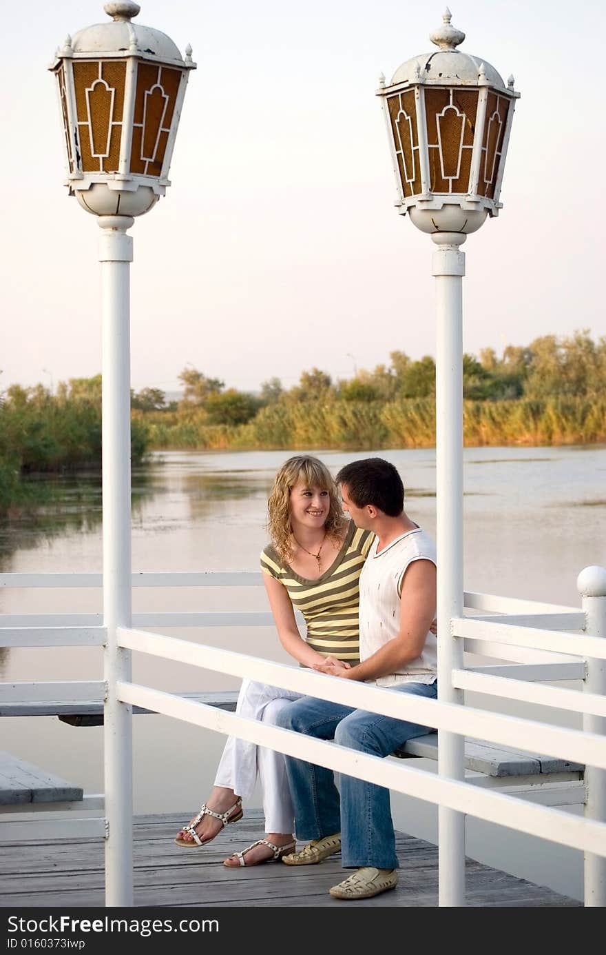 Pair on a pier. Look against each other and smile