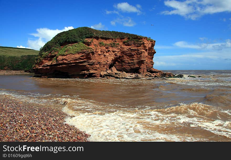 Pebble beach, the incoming tide and grass topped triassic era mudstone cliff headland photographed on a summers day at Budleigh Salterton Devon England