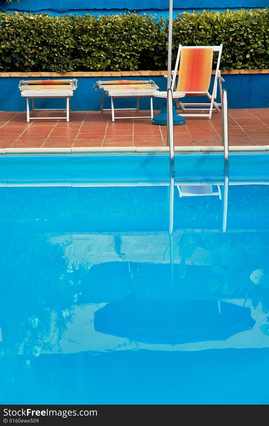 Hotel swimming pool with reflection and deck-chairs. Shallow depth of field