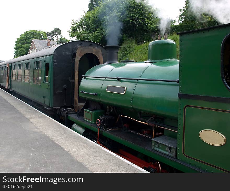 A green steam train and carriage at a station