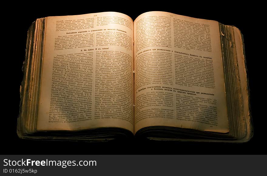 Old open book isolated on black in candlelight.