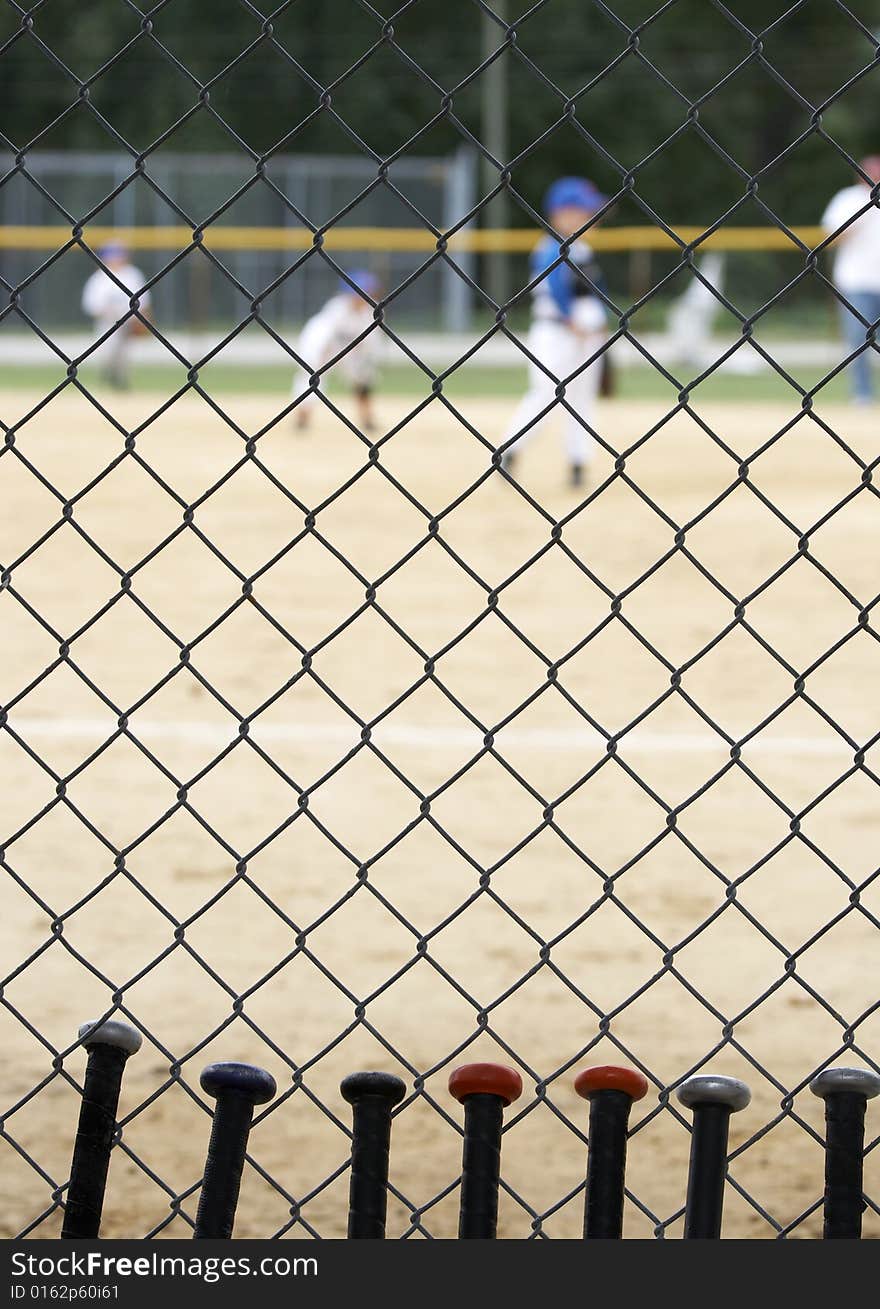 Baseball bats learning against dugout fence as game is played. Baseball bats learning against dugout fence as game is played