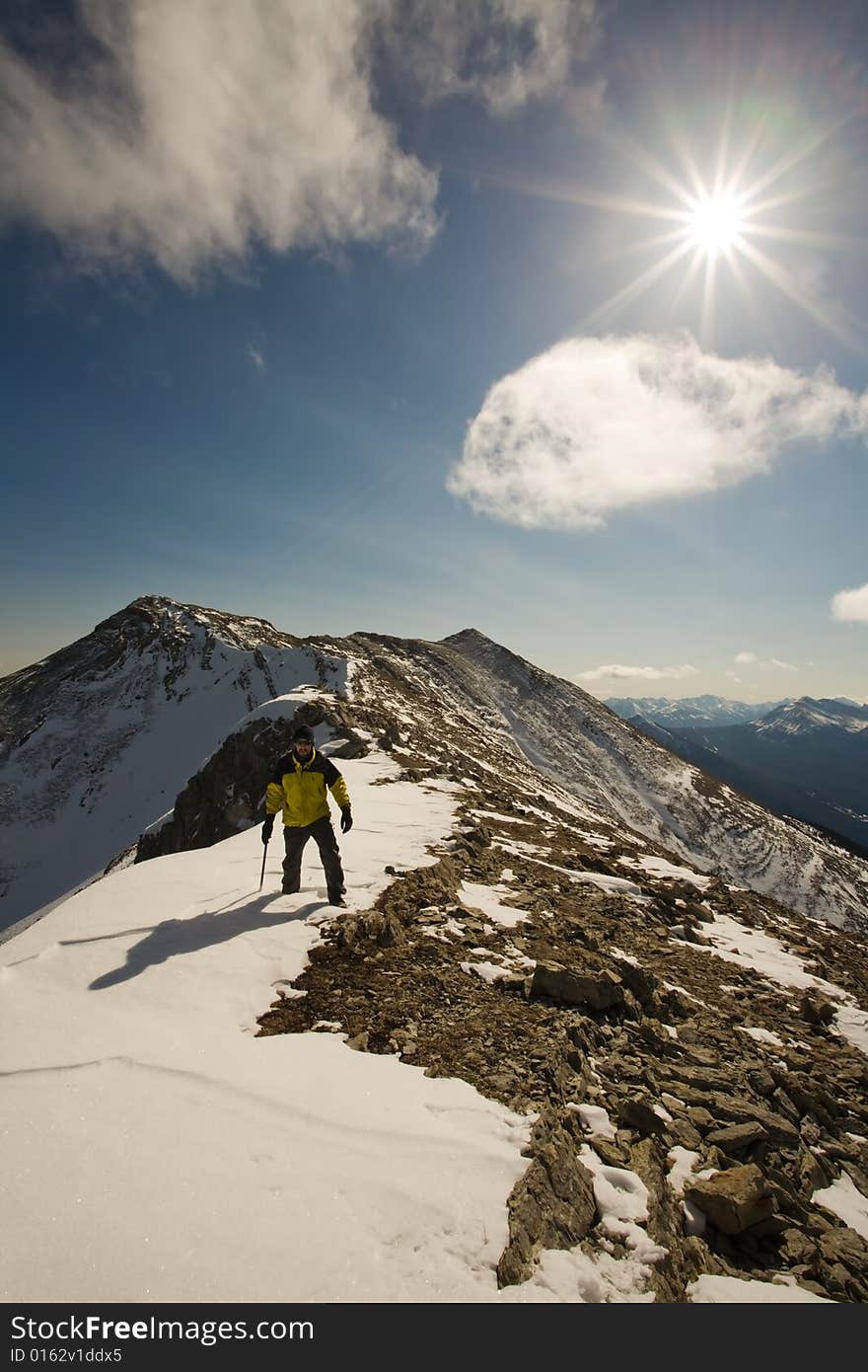 Climber beneath the sunshine on snowy, rocky, exposed summit ridge of mountain. Climber beneath the sunshine on snowy, rocky, exposed summit ridge of mountain