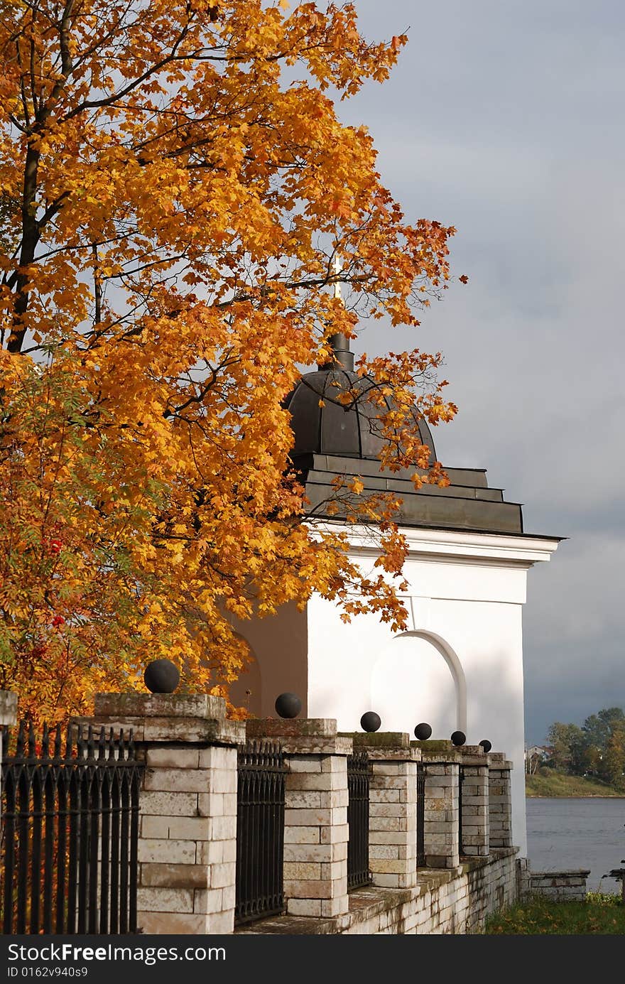 Dome of chapel with a gold cross and tree with an autumn foliage