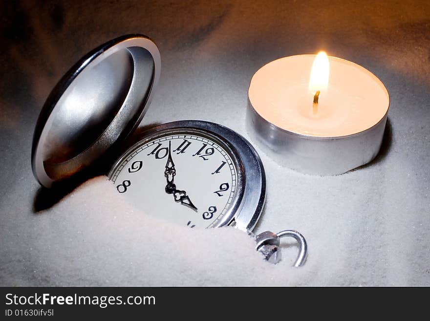 Antique watch covered with sand and a candle